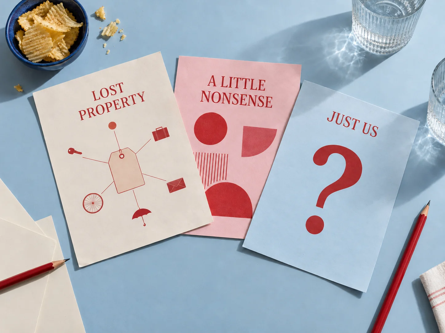 Printed mystery and party-game covers laid out on a blue table with pencils, drinks and snacks.